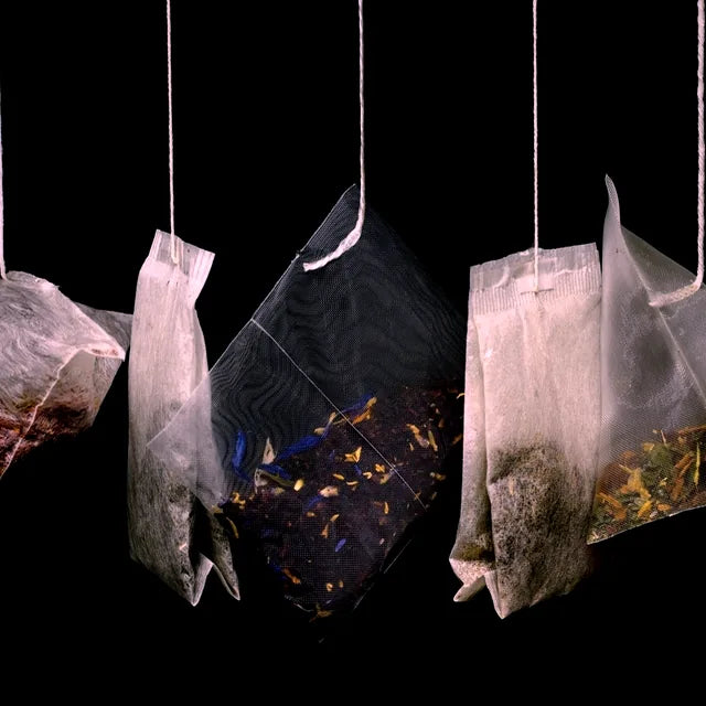 Hand-filled herbal tea bags hanging against a black background