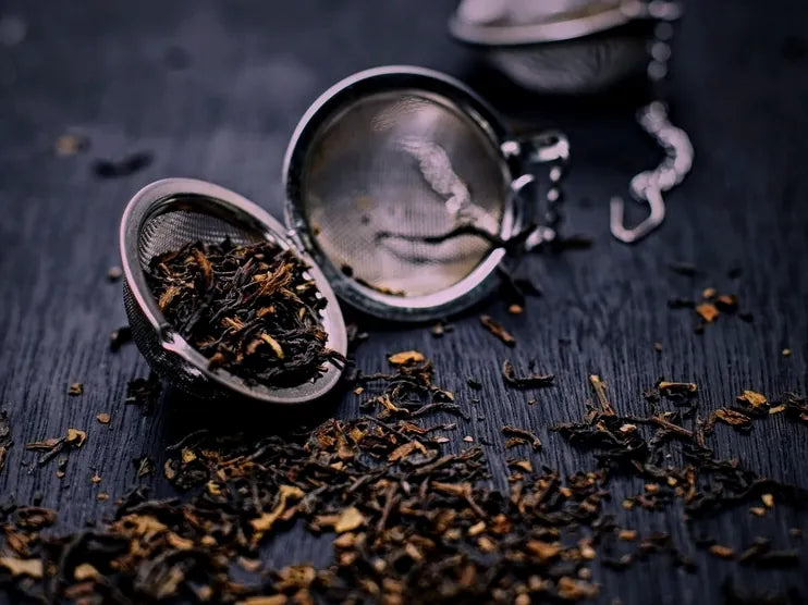 Loose herbal tea leaves spilling from an infuser on dark wood